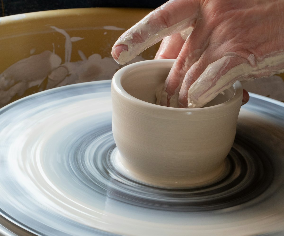 Hands shaping a small pot on a potter's wheel