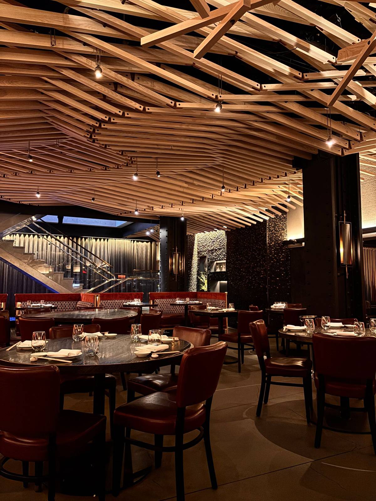 The dining room at night: round tables, red leather chairs and a wooden ceiling